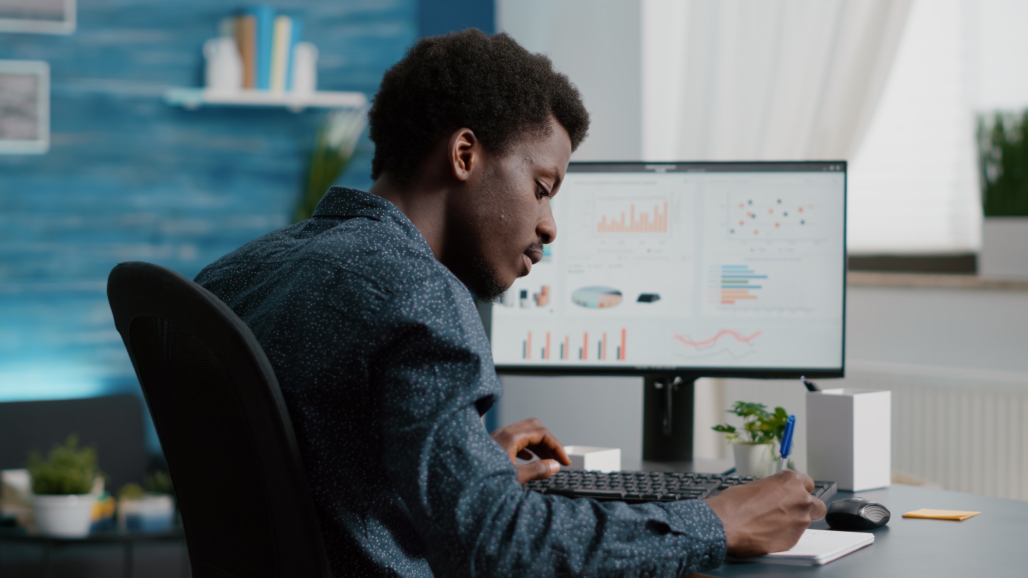 Selective focus on black american guy working from home, taking notes on paper notepad